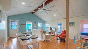 A spacious living room with a wooden floor, a ceiling fan, and a dining area with a table set for four. - Port A Cottage by Avantstay Private Patio + Deck Designed for Groups (Port Aransas)