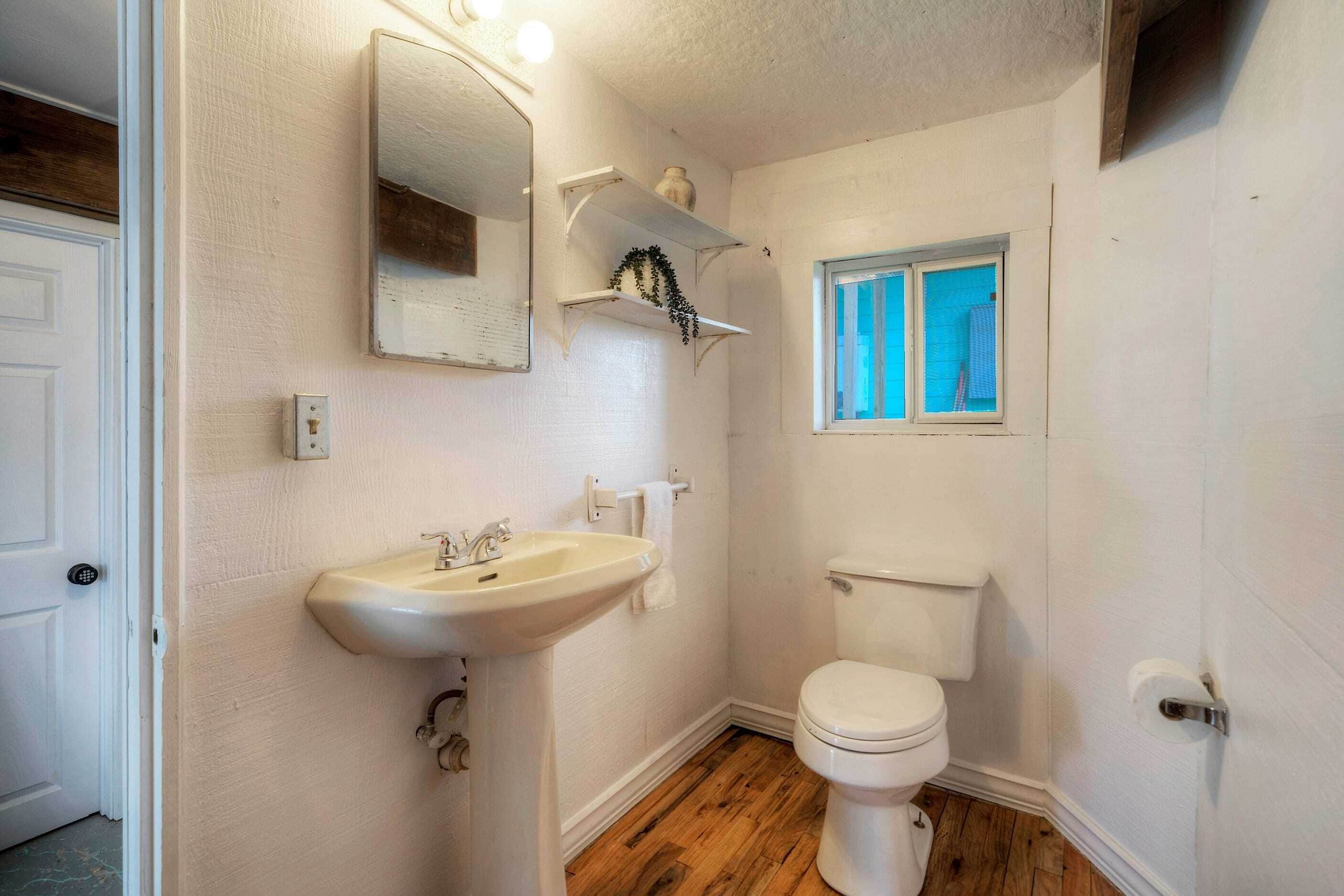 A bathroom with a white sink, a toilet, a window, and a mirror.