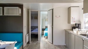 A compact hotel room with a kitchenette, a bed with a blue cover, and a small bathroom.
