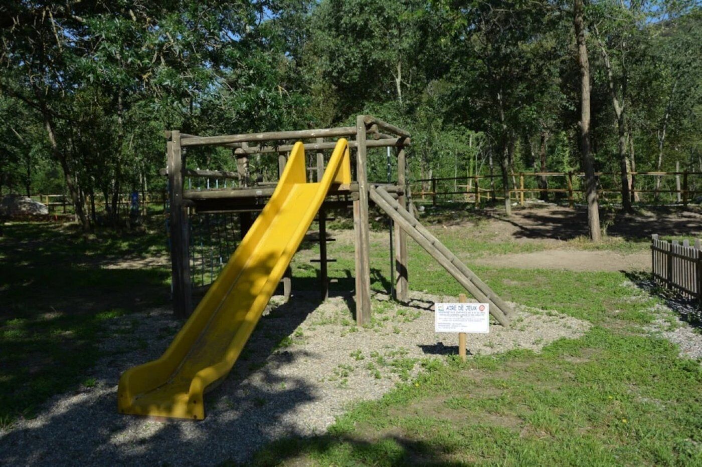 A playground with a yellow slide and a wooden climbing structure.