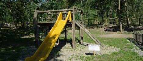 A playground with a yellow slide and a wooden climbing structure.