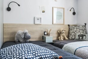 Une chambre avec deux lits, une table de chevet, des lampes fixées au mur, des œuvres d’art encadrées et des coussins décoratifs.