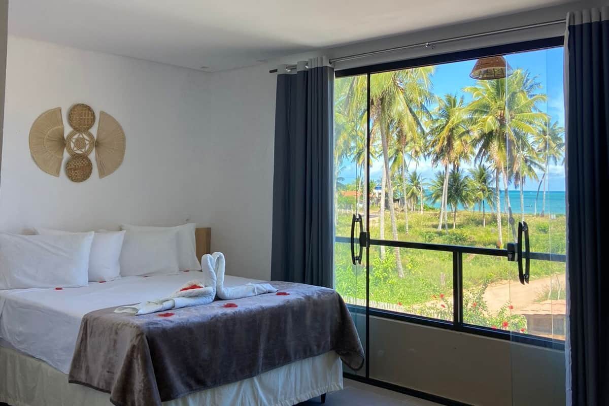 Ein Schlafzimmer mit Bett, Blick auf Palmen und Meer, sowie einer Deckenleuchte.