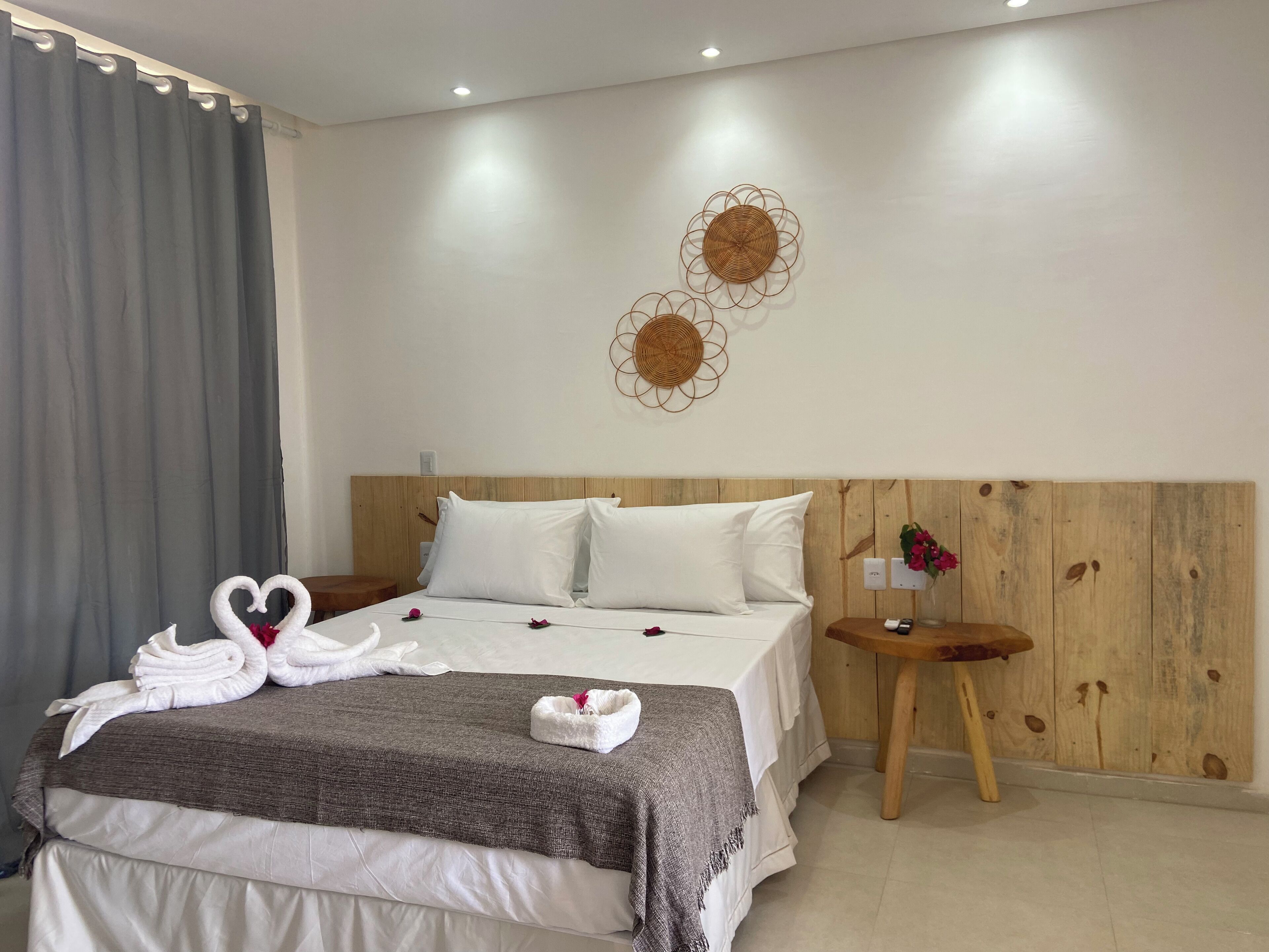 A neatly made bed with white linens and a gray blanket, a wooden headboard, a small wooden nightstand with a vase of flowers, and a wall with decorative circular wall art.
