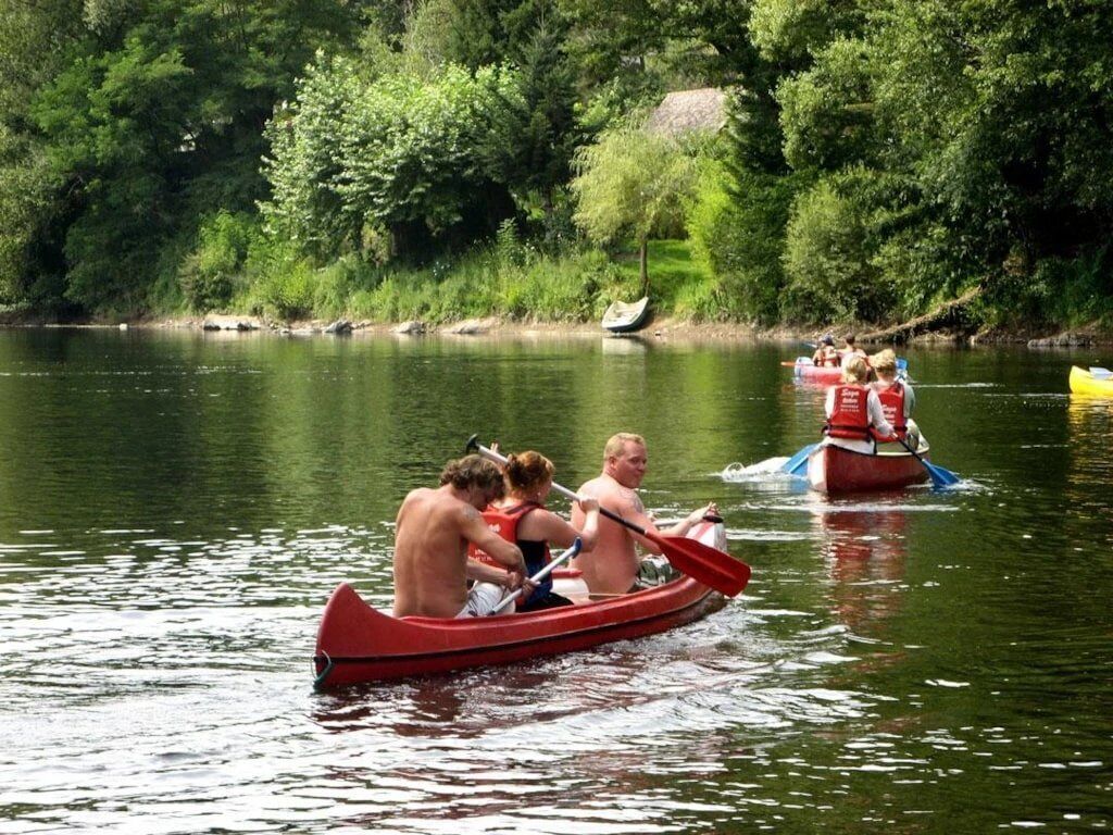 Un groupe de personnes se trouve dans un canoë rouge sur une rivière paisible, entourée d’une végétation luxuriante.