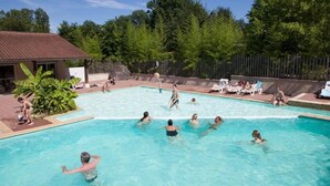 Ein Schwimmbecken mit darin badenden Personen, umgeben von Bäumen und einem eingezäunten Bereich mit Liegestühlen.