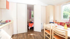 A compact kitchen with a dining area, wooden cabinets, and a window providing natural light. - ZEcamping 4* animé 3km plage piscine chauffée tente TV BBQ clim 16m2 (Canet-en-Roussillon)