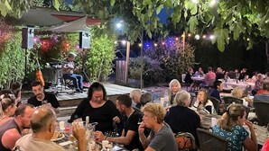 An outdoor dining area with tables and chairs, surrounded by greenery and string lights.