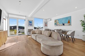 Ein modernes Wohnzimmer mit einer großen Eckcouch, einem Esstisch mit Stühlen und einem Bild an der Wand.