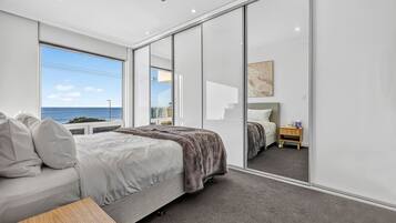 A modern bedroom with a large bed, a bedside table, a nightstand, and a view of the sea.