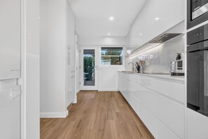 A modern kitchen with white cabinetry, a wooden floor, and a view through a glass door to an outdoor area.