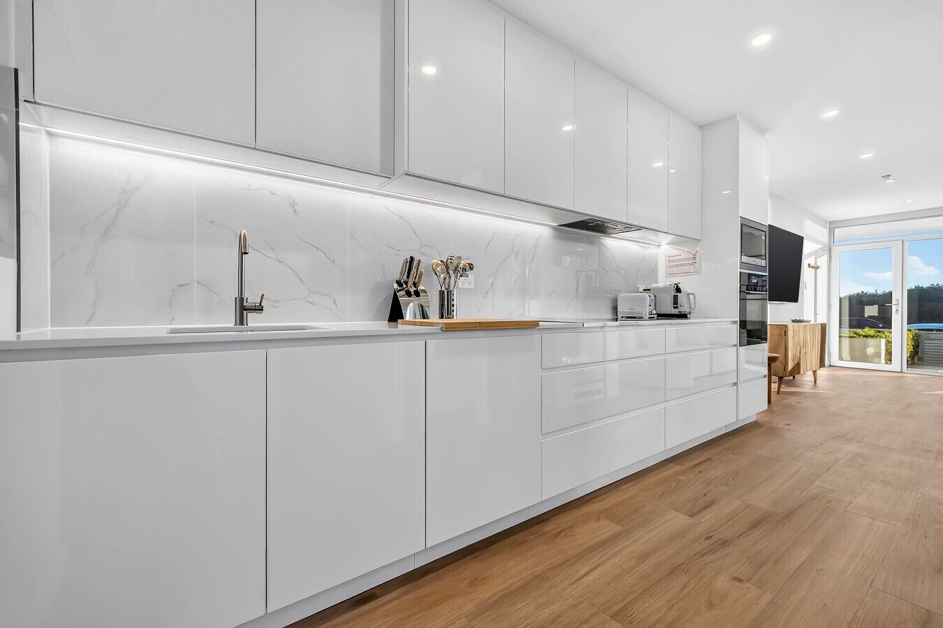 A modern kitchen with white cabinetry, a marble backsplash, and a wooden floor.