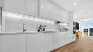 A modern kitchen with white cabinetry, a marble backsplash, and a wooden floor. - Sunset Sands on Esplanade | By Host Solutions (West Beach)