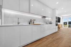 A modern kitchen with white cabinetry, a marble backsplash, and a wooden floor.