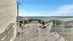 A balcony with a glass railing, white plastic chairs, and a table. - Sunset Sands on Esplanade | By Host Solutions (West Beach)
