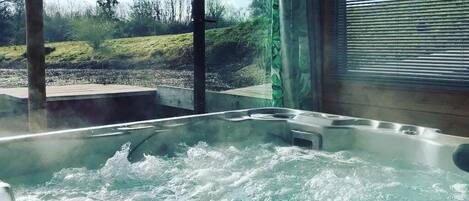 Un jacuzzi con vistas a un paisaje cubierto de hierba a través de amplias ventanas.