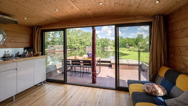 A spacious room with a wooden ceiling, a large sliding glass door leading to an outdoor area with a table and chairs, and a sofa with a cushion. - ZEcamping piscine chauffée jacuzzi sauna locatif BBQ clim 25m2 6 pers (Chassenard)