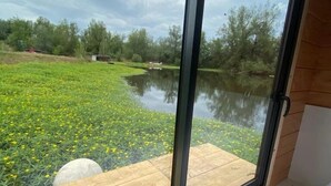 A room with a large window overlooking a grassy area with a pond and trees. - ZEcamping piscine chauffée jacuzzi sauna locatif BBQ clim 25m2 6 pers (Chassenard)