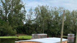 A wooden floating houseboat with a small deck, windows, and a chimney. - ZEcamping piscine chauffée jacuzzi sauna locatif BBQ clim 25m2 6 pers (Chassenard)