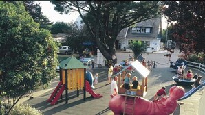 Un parque infantil con un tobogán, una estructura de escalada y una zona de juegos con una gran estatua de elefante rosa.