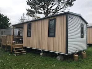 Une maison mobile de plain-pied, avec une façade en bois, une véranda dotée de marches et une bouteille de propane visible.