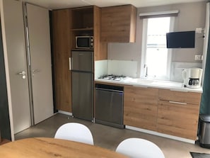 Une cuisine compacte dotée de meubles en bois, d’un four à micro-ondes, d’un réfrigérateur, d’un lave-vaisselle, d’une cuisinière à gaz et d’une fenêtre avec des stores.