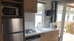 Una cocina compacta con refrigerador de acero inoxidable, microondas y lavavajillas. Hay un ventanal sobre el fregadero y un televisor montado en la pared.
