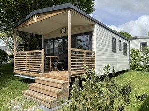 Une maison mobile dotée d’un porche couvert, d’une petite terrasse et d’une partie avant avec des fenêtres.