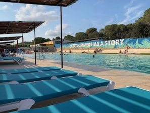 Une piscine dotée de chaises longues et d’une fresque murale portant l’inscription : « CHAQUE ÉTÉ A SON HISTOIRE ».