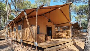 Una cabaña de madera rústica con un porche grande y una terraza cubierta, rodeada de árboles.