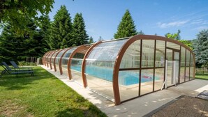 A covered swimming pool with a transparent roof, surrounded by a grassy area and trees. - ZEcamping 3 étoiles piscine couverte animaux acceptés locatif clim (Chamberet)