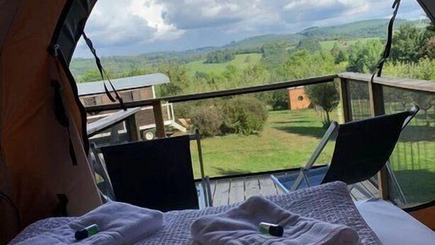 Ein Zelt mit einem Bett, zwei Stühlen und Blick auf eine grüne Landschaft.