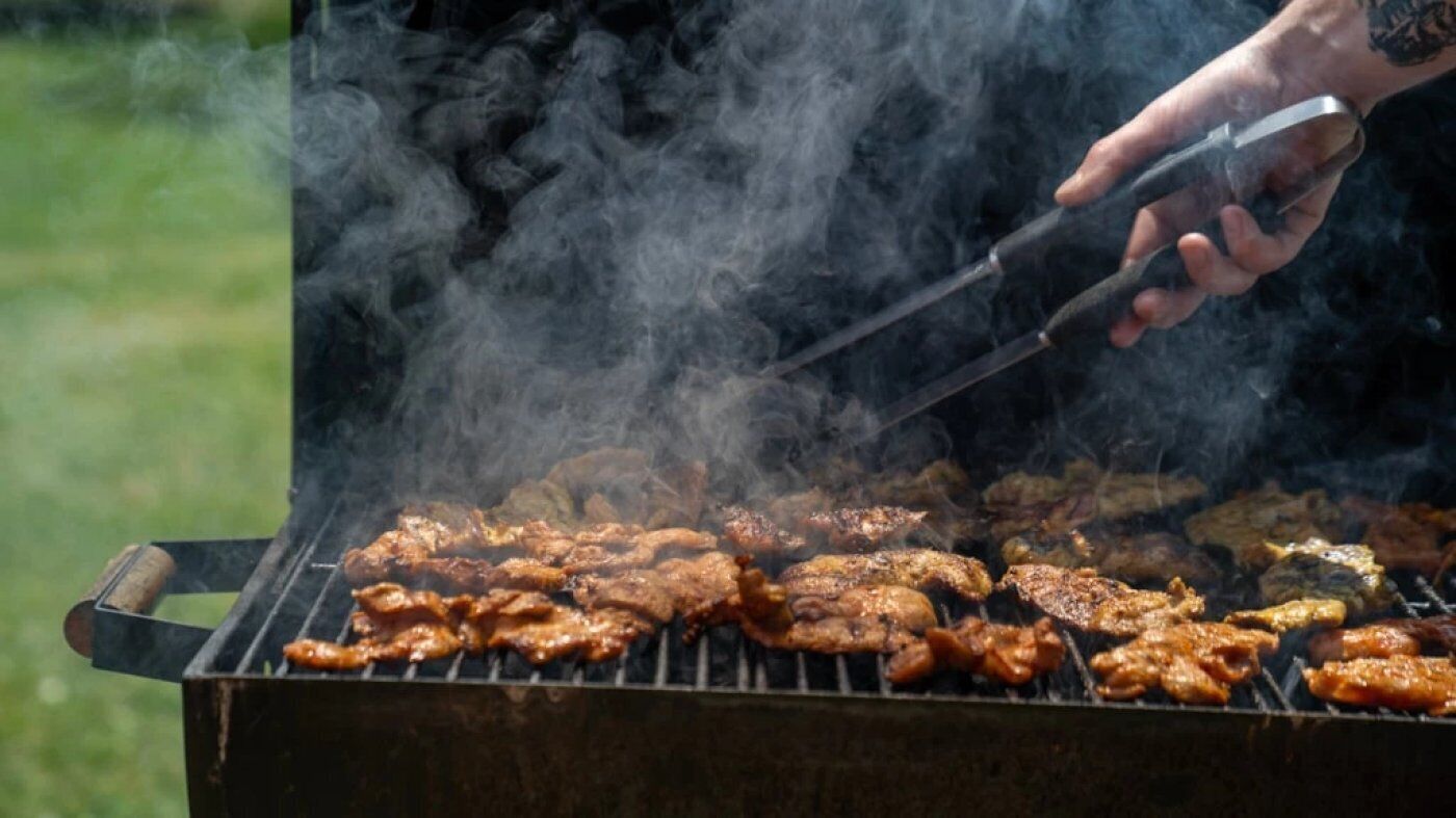 Eine Person grillt verschiedene Fleischsorten auf einem Grill im Freien.