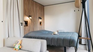A modern bedroom with a large bed, a sofa, a decorative hat on the bed, and a wall-mounted lamp.