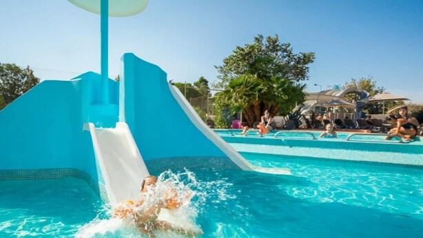 A swimming pool with a water slide and a poolside area with lounge chairs.