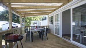 A covered deck with a table and chairs, a grill, and a glass door leading to a house.