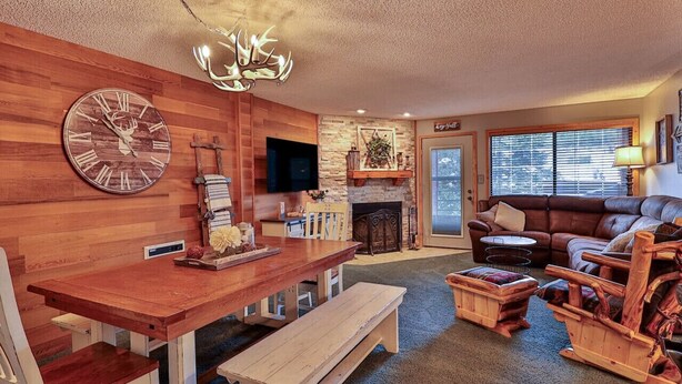 A cozy living room with a wooden wall, a large clock, a fireplace, a sofa, and a television.