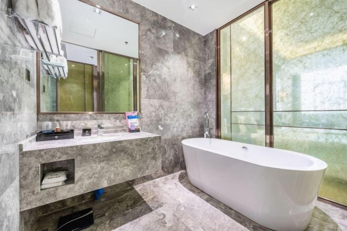 Un baño moderno con una bañera independiente, paredes de mármol y un espejo grande.