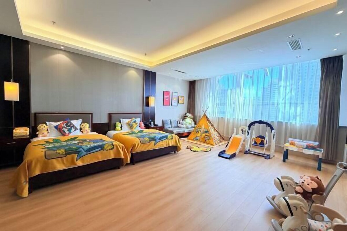 A hotel room with two beds, a desk, a chair, a window, and a tent-like play area.