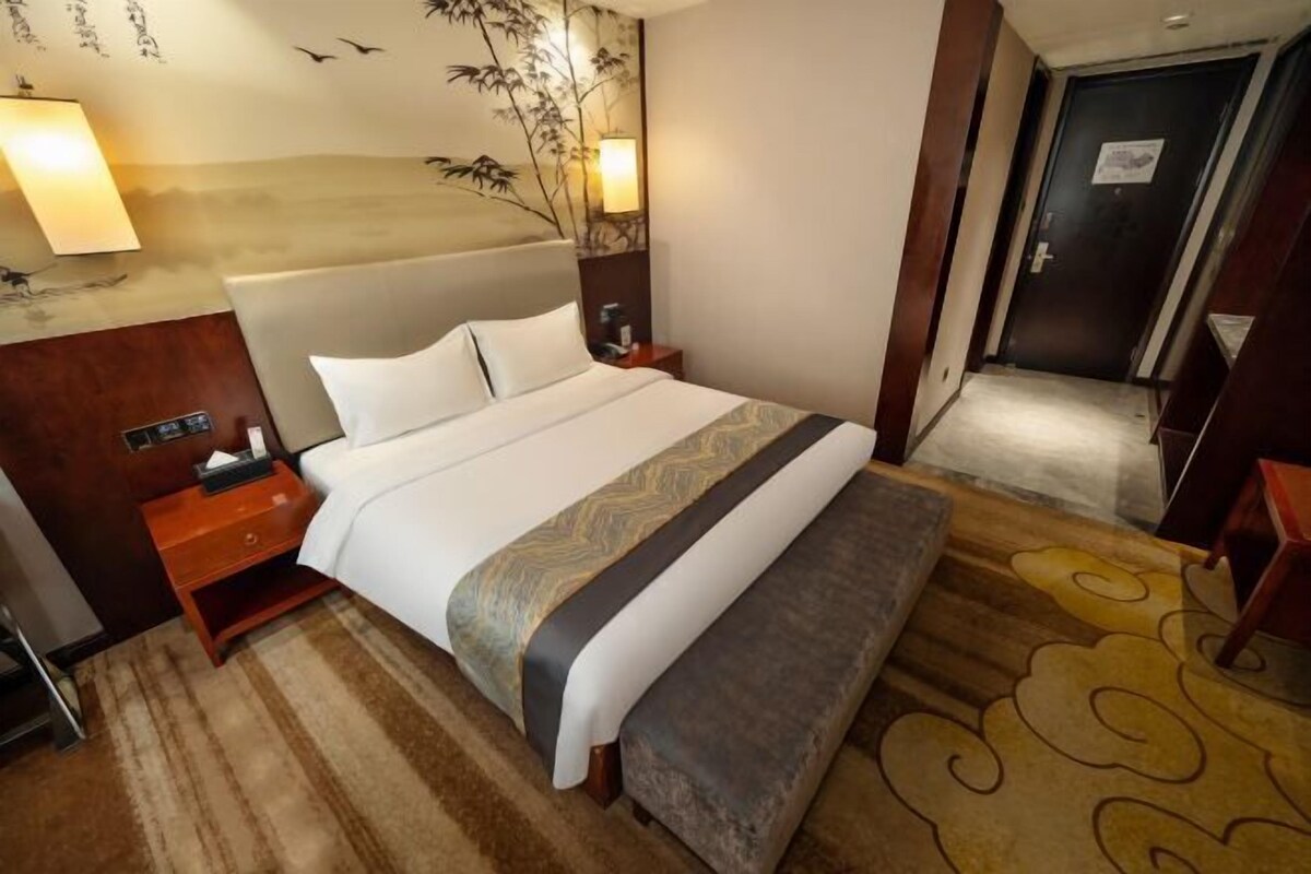 A hotel room with a large bed, a nightstand, a lamp, and a wall with a bamboo design.