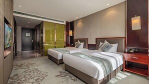 Ein Hotelzimmer mit zwei Betten, einem Holznachttisch, einem Schreibtisch und einem großen Fenster.
