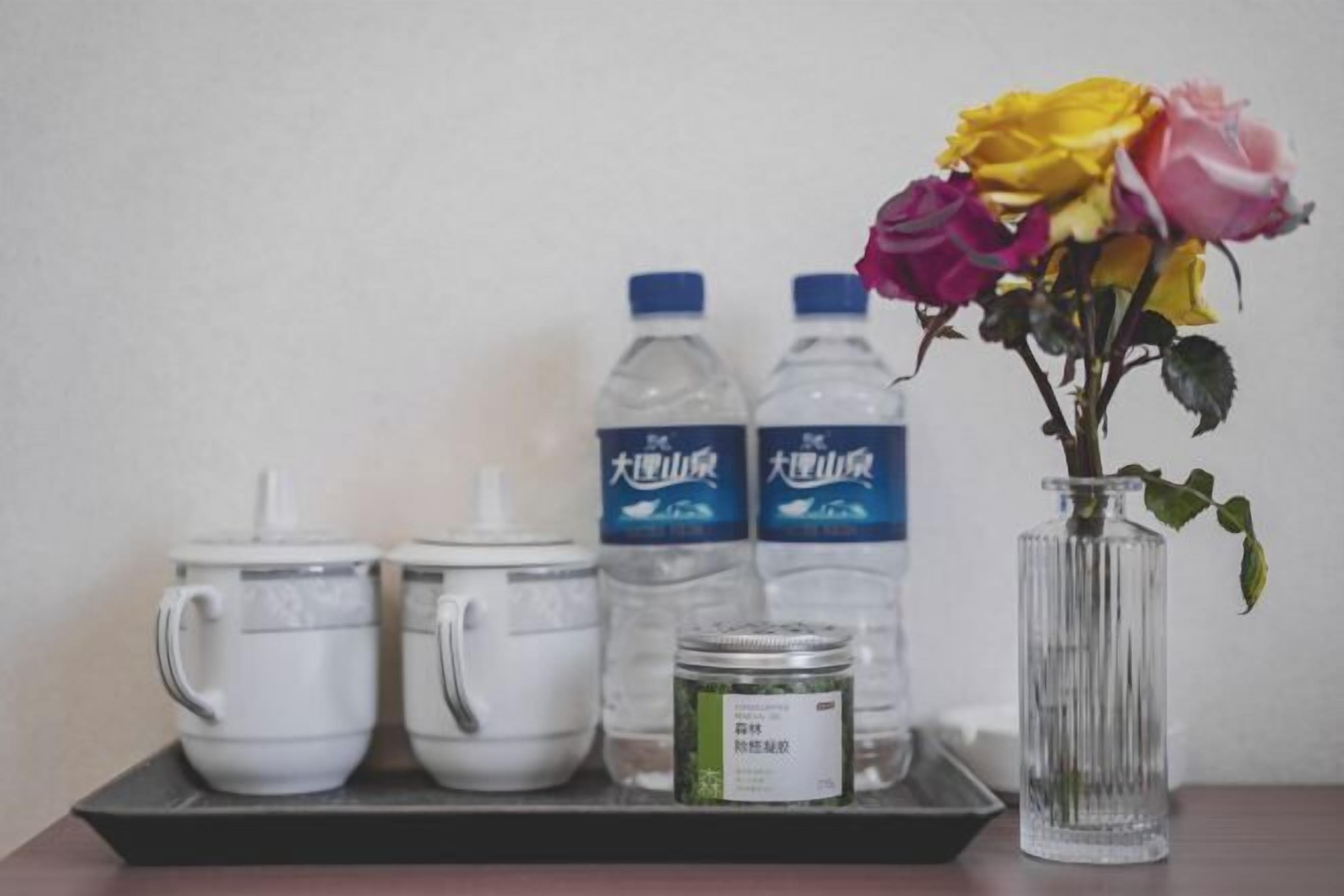 A tray with two white teapots, two water bottles, a jar of tea, and a vase with roses.