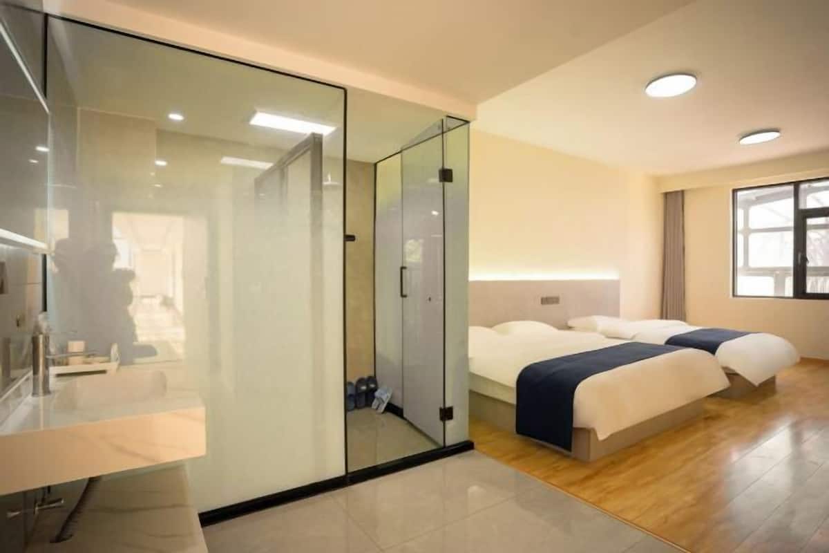 Een moderne hotelkamer met een glazen scheiding tussen de badkamer en slaapkamer, een groot bed met hoofdeinde, en een raam voor natuurlijk licht.