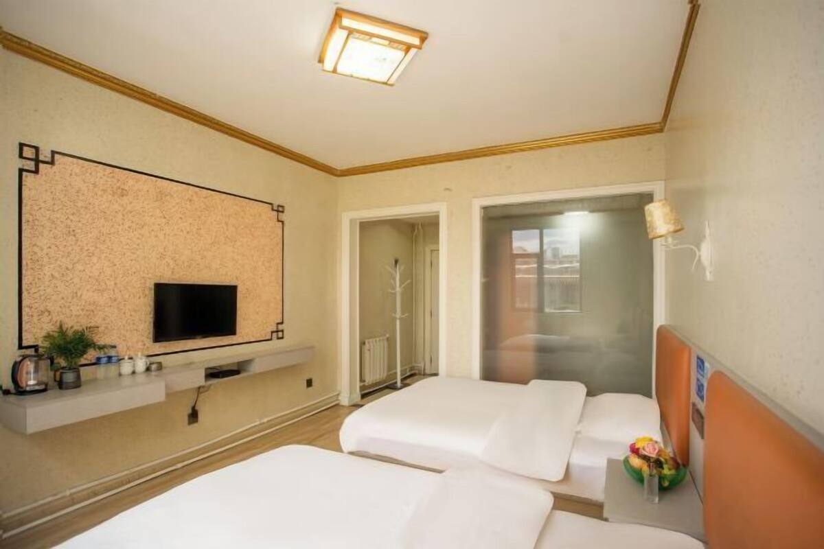 Een hotelkamer met een televisie, twee bedden, een douchegedeelte en een kleine plant.