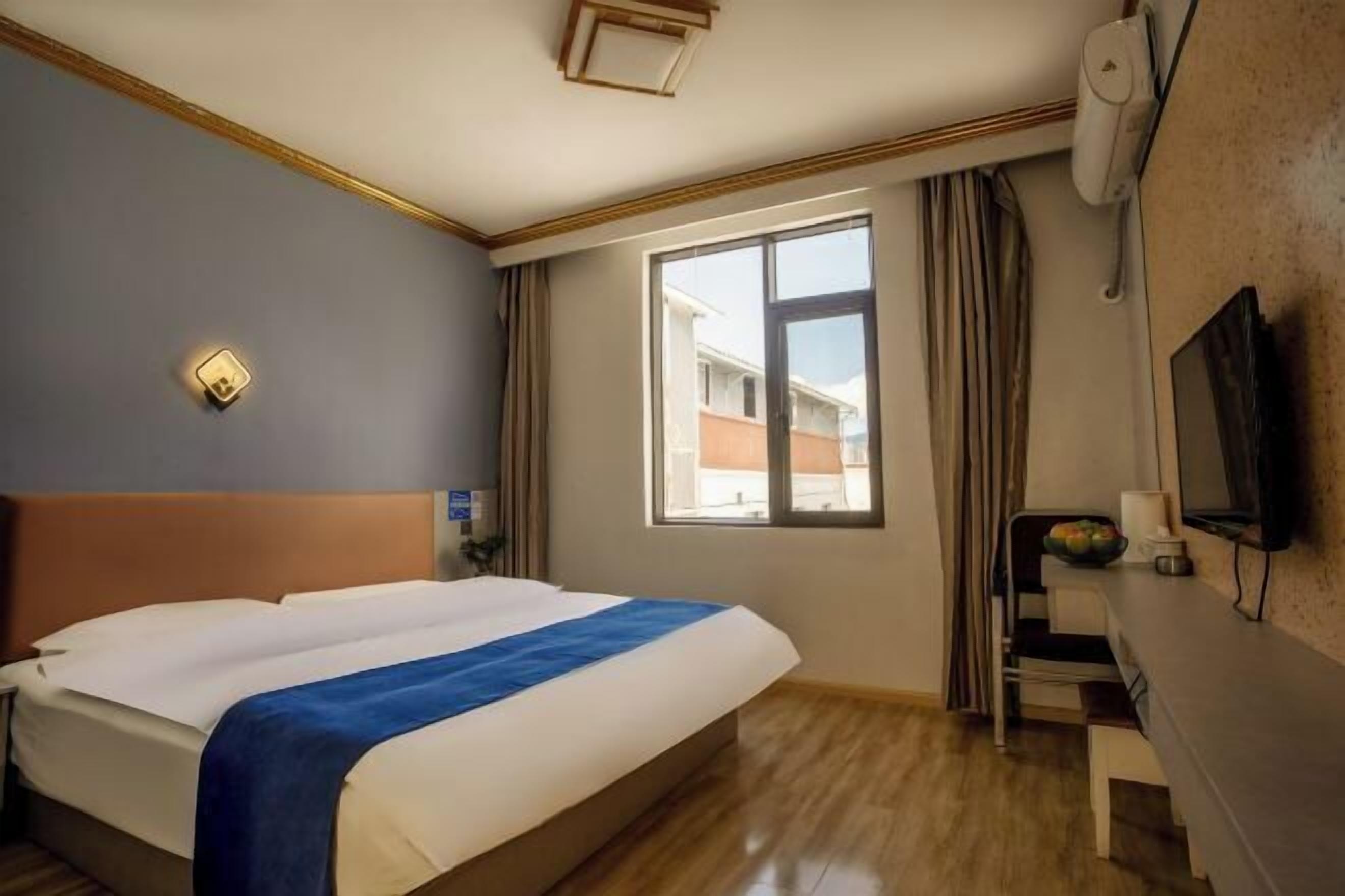 Una habitación de hotel con cama, escritorio, televisión y ventana con cortinas.