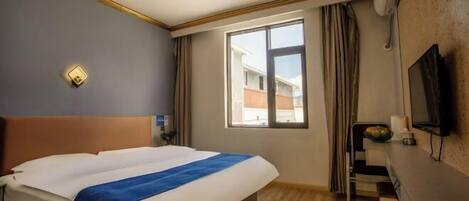 Una habitación de hotel con cama, escritorio, televisión y ventana con cortinas.