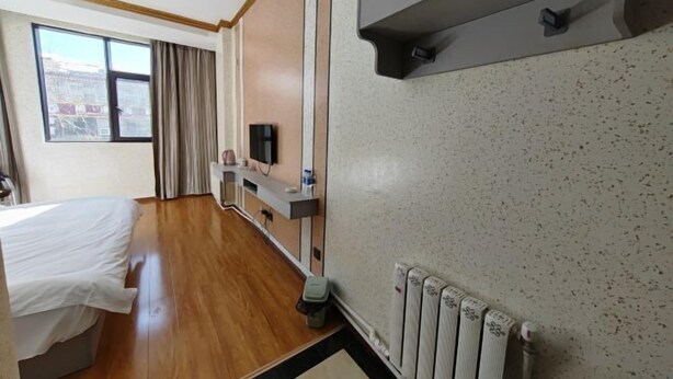 Une chambre d’hôtel avec un lit, une télévision, une petite table avec une bouteille, un radiateur et une fenêtre avec des rideaux.