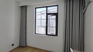 Une pièce dotée d’une grande fenêtre, de rideaux gris et d’un plancher en bois.
