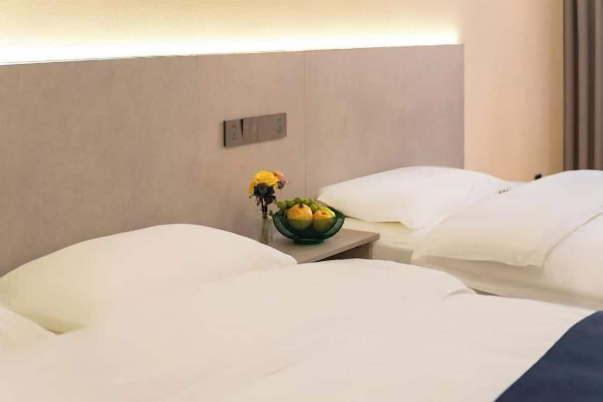 Een hotelkamer met twee bedden, een nachtkastje met een schaal fruit en een wandlamp.