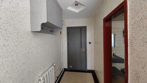 Un couloir étroit avec un radiateur, une porte grise et une porte à cadre rouge qui donne sur une autre pièce.